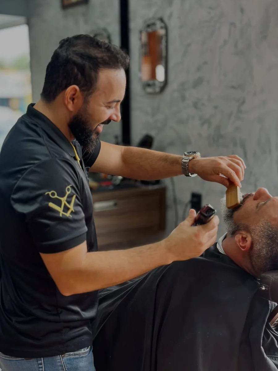 Barbeiro da Fino Trato sorrindo enquanto apara a barba de um cliente
