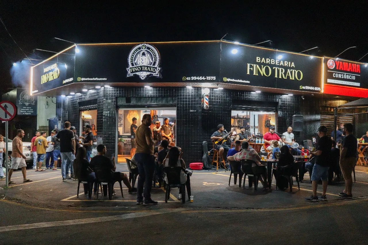 Fachada da Fino Trato iluminada na noite de inauguração, com convidados na calçada