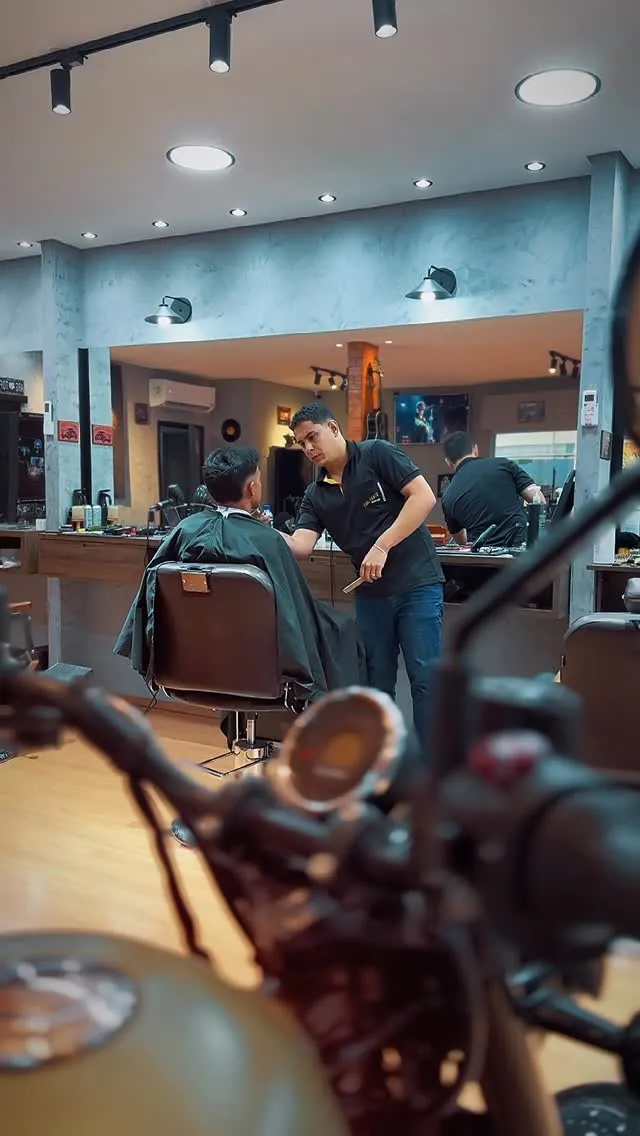 Salão da Fino Trato visto por trás do guidão da moto em exposição, com um barbeiro atendendo